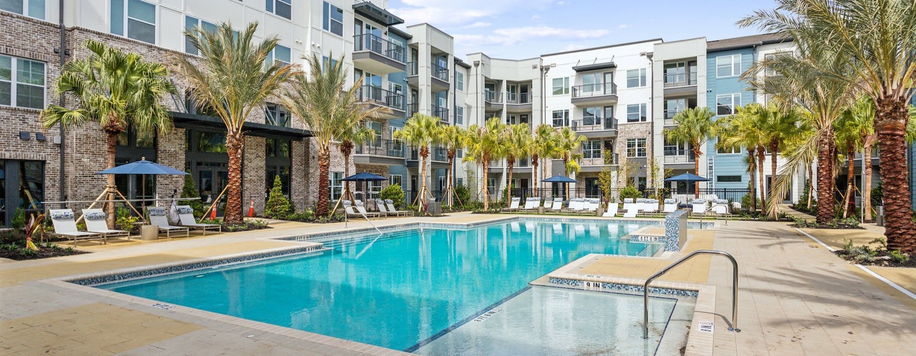a pool in a courtyard with palm trees and buildings in the background